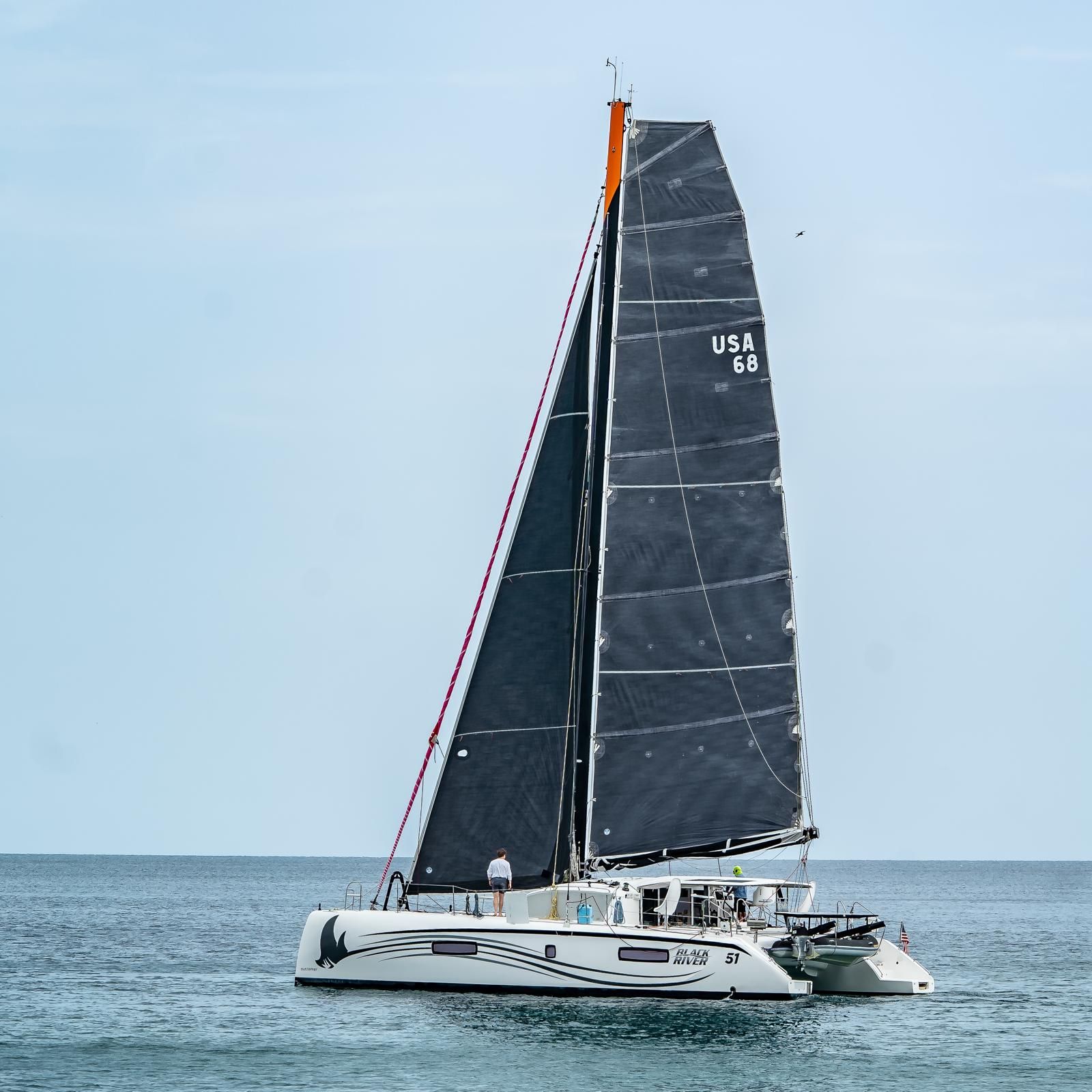 The catamaran Black River under dark sails on a calm sea